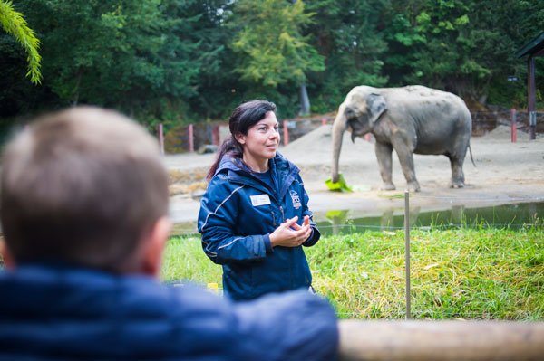 Woman talking to a crowd with an elephant in the background.